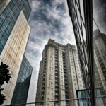 Low angle view of contemporary skyscrapers with glass facades under a cloudy sky.